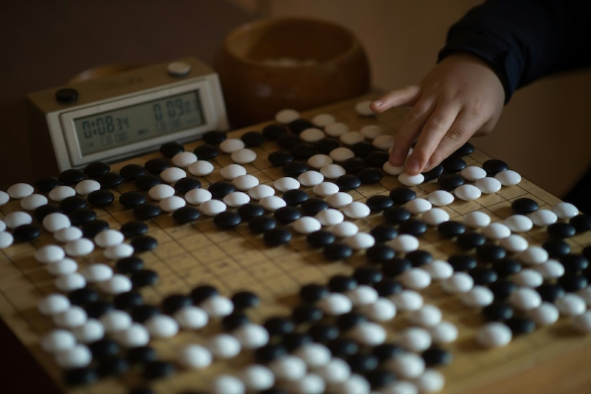 a person's hand can be seen touching a stone on a Go game board
