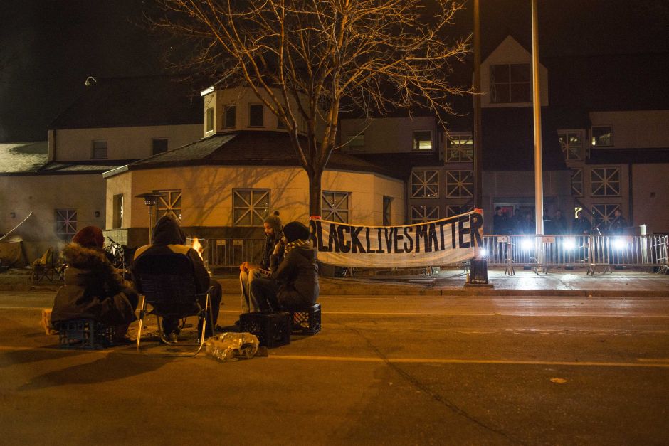 A group sits outside of the police station after five people were shot