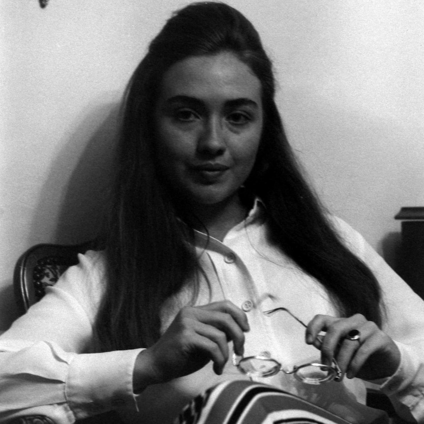 a black and white photo of a young woman holding her glasses