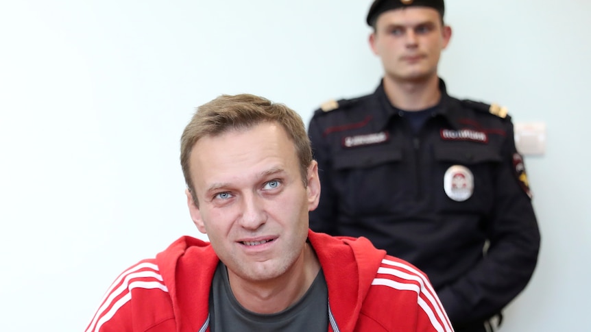 Uśmiechnięty Aleksiej Nawalny jest sfotografowany w moskiewskim sądzie z policją za nim na tym zdjęciu z akt z 2019 roku.