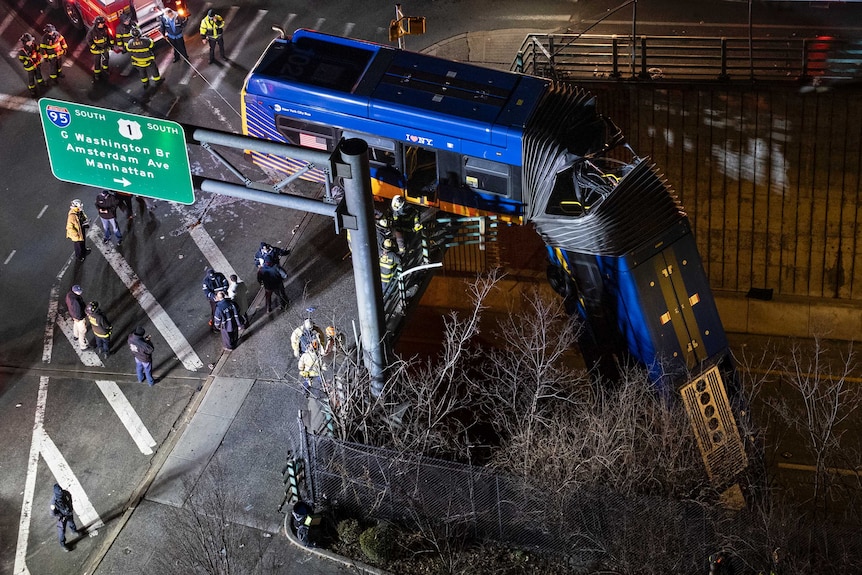 A blue bus hangs over an overpass.