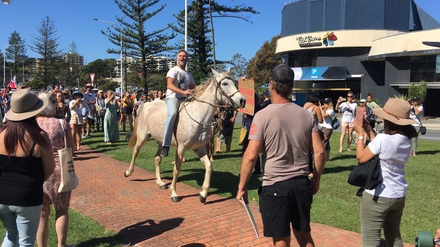 A man rides a horse through a large crowd in a seaside area.