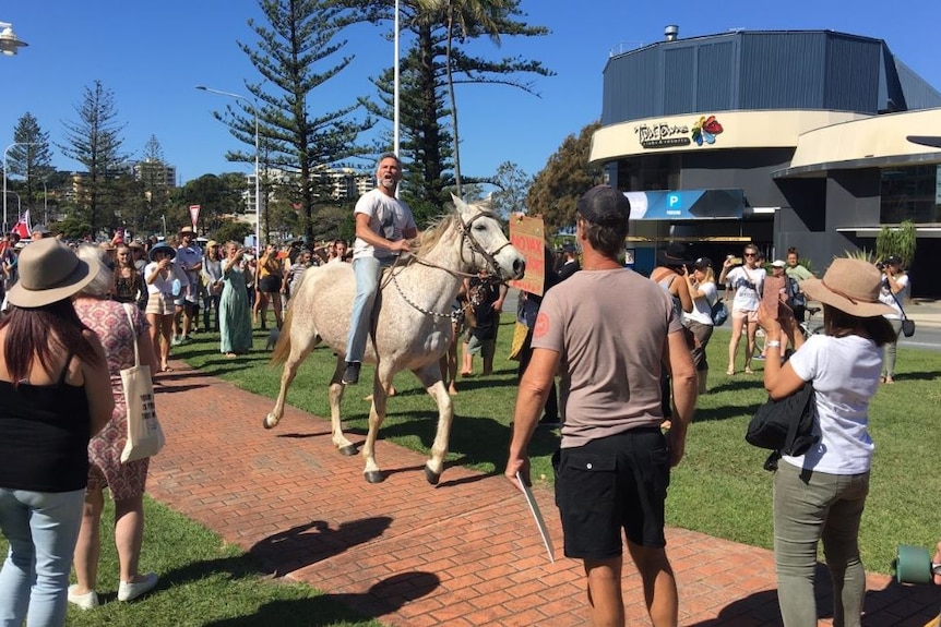 A man rides a horse through a large crowd in a seaside area.