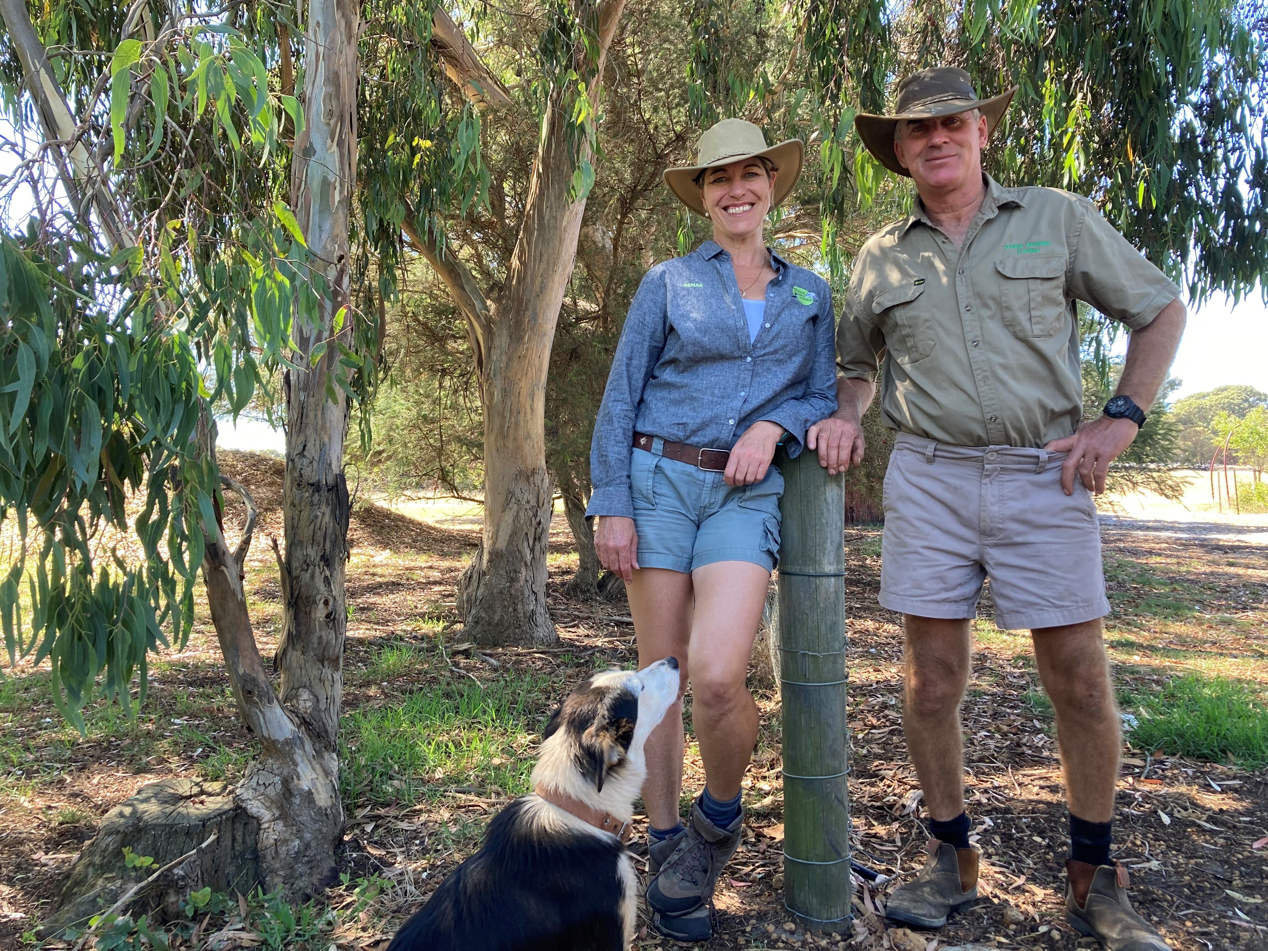 Man, woman and dog pose for photo near fence on farm