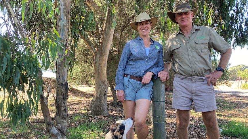 Man, woman and dog pose for photo near fence on farm