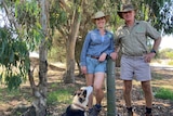 Man, woman and dog pose for photo near fence on farm