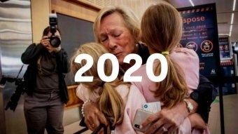 A woman hugs two young girls at an airport. Text saying 2020 is imposed on top