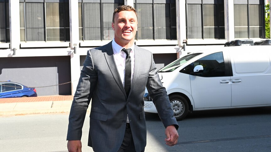 Jack Wighton wearing a grey suit smiling as he walks along. 