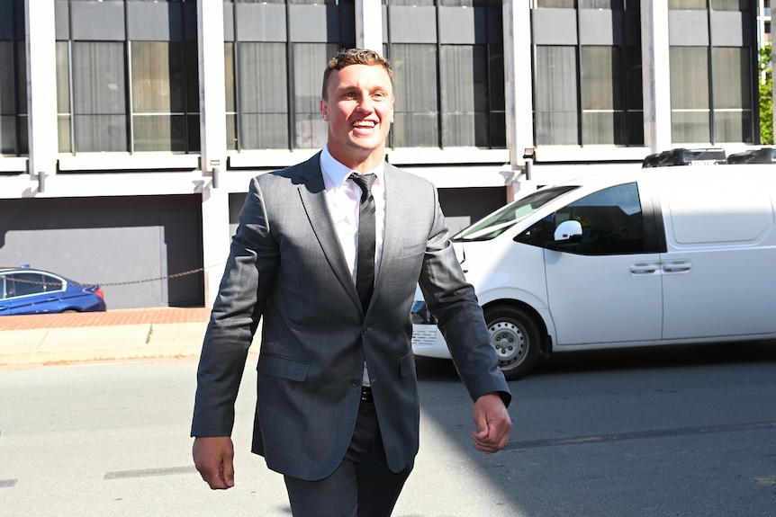 Jack Wighton wearing a grey suit smiling as he walks along. 