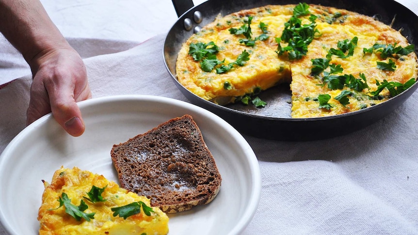 A slice of frittata in a bowl with bread alongside a pan of frittata, a quick meal for a weekend brunch.