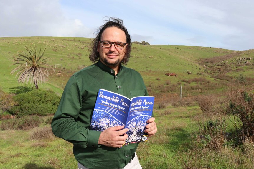 Man in middle of frame holding a book with green paddock in backgound