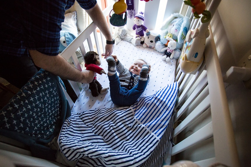 Baby Oskar playing with a monkey toy in a cot.