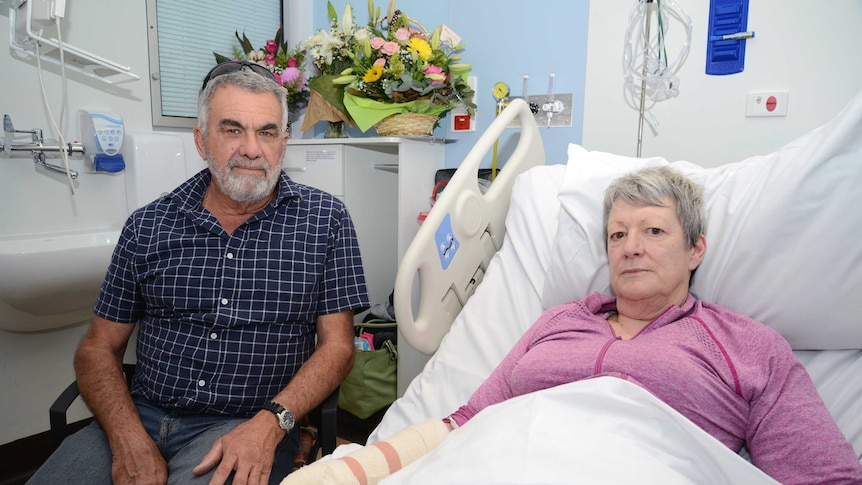 Gail Linton in a hospital bed with bandages on one hand and arm.