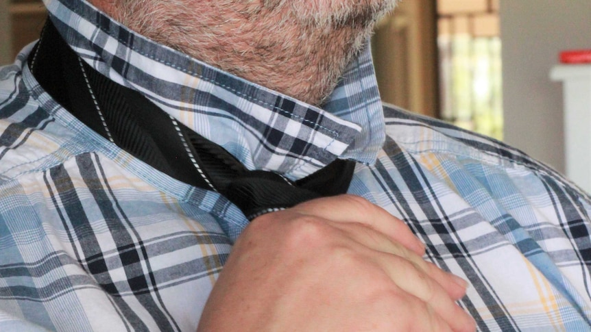 A man knotting a tie at his neck.