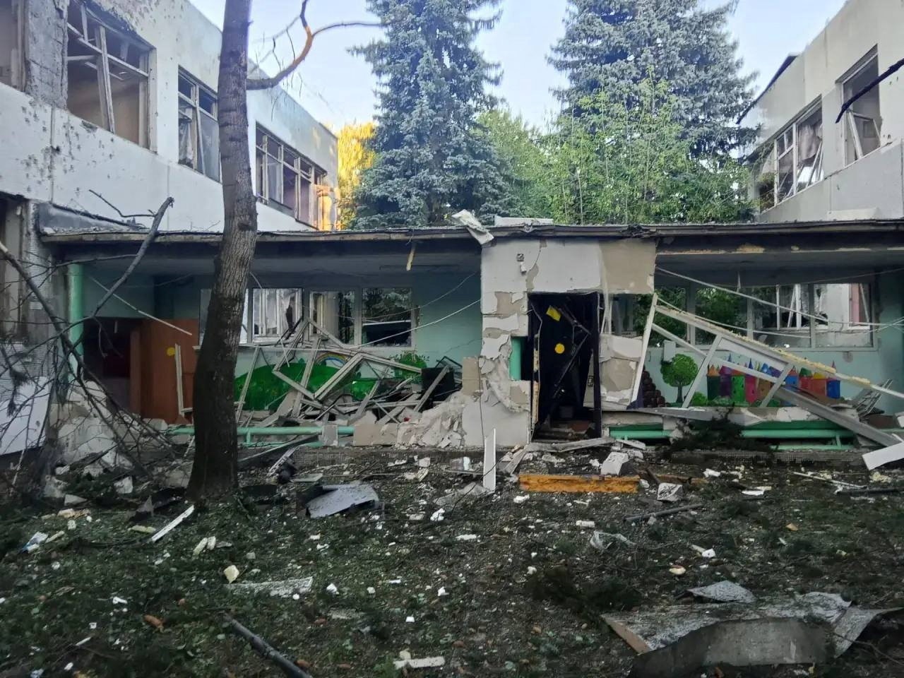 A connecting corridor between two buildings is badly damaged, with smashed windows and debris on the ground.