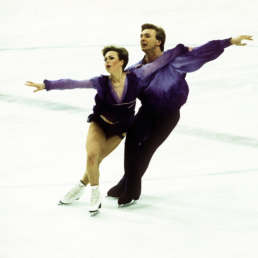 Ice dancers glide on the ice wearing matching purple costumes. 