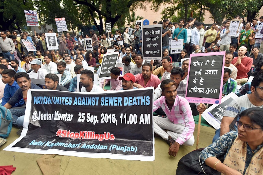 Crowd holds signs in protest of manual scavenging.