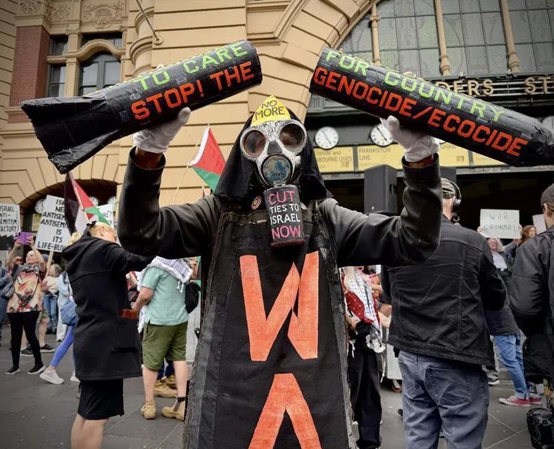 Una persona disfrazada, con una máscara antigás y agitando carteles que decían 