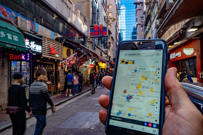 A man's hand holding a phone up in a Hong Kong street