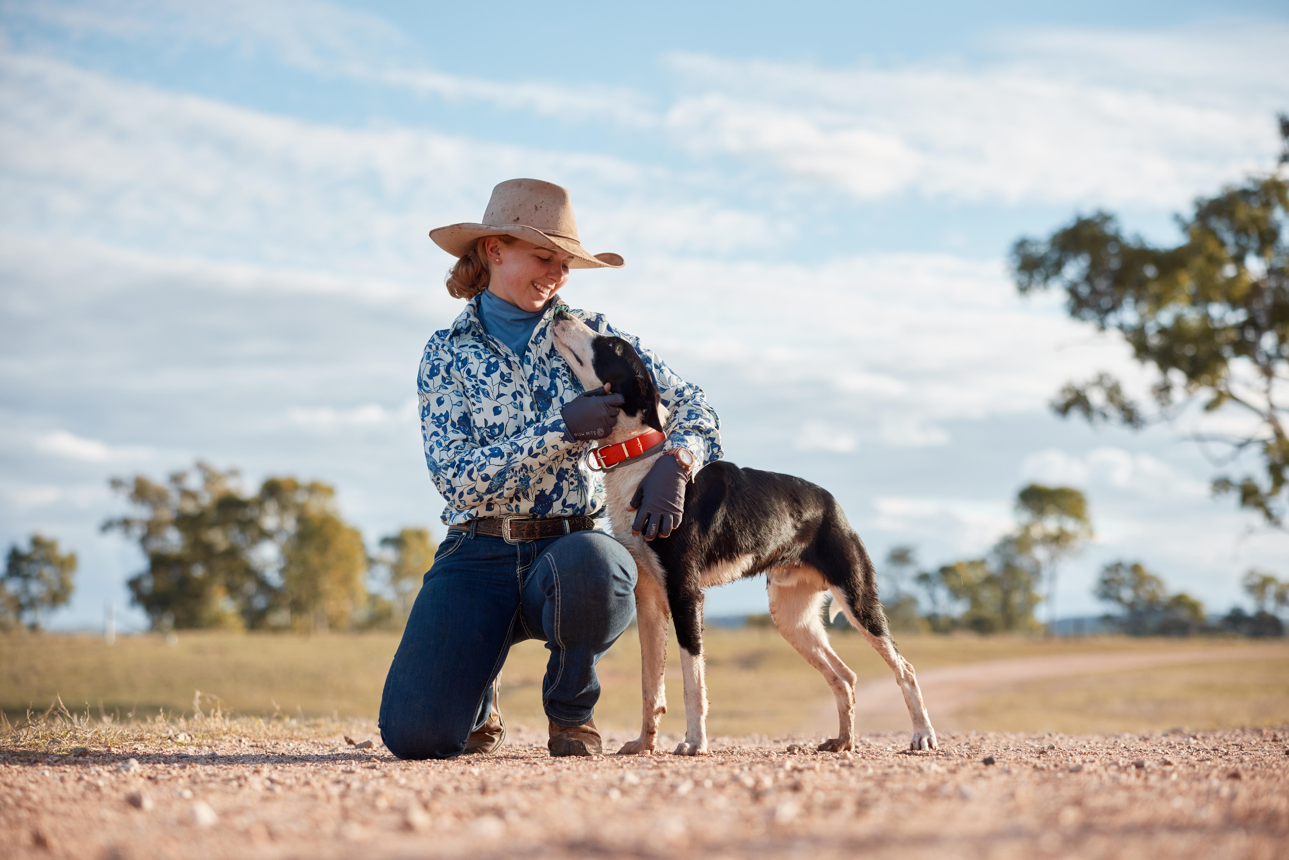 A smiling young woman cuddles a dog on a country property.