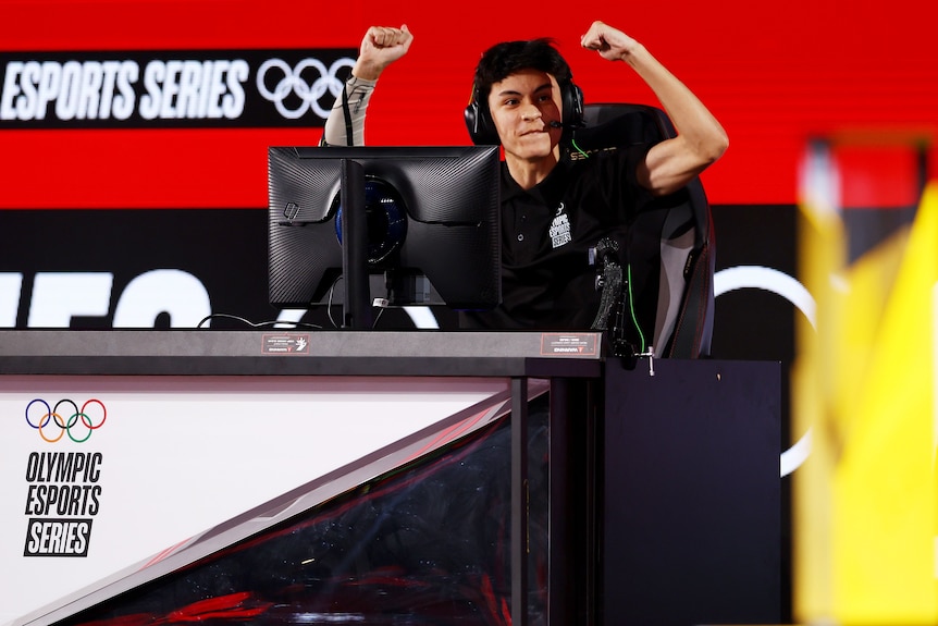 a video gamer with a head set celebrating in front of a computer screen on stage