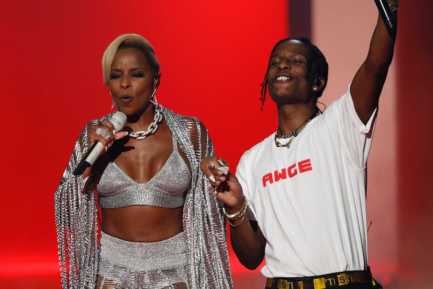 A$AP Rocky raises his microphone in the air on a stage with Mary J Blige