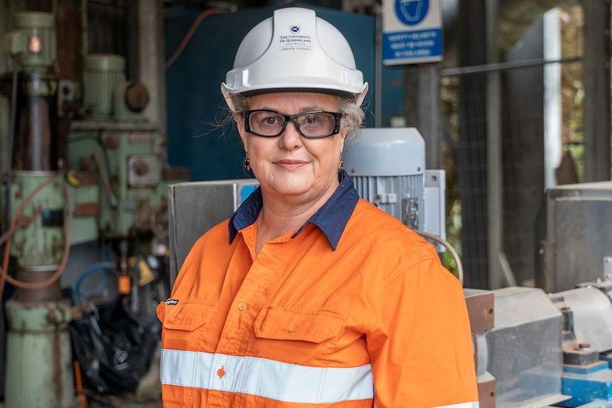 Professor Alice Clark, geologist, stands in a hard hard and high-vis work wear at a work site.