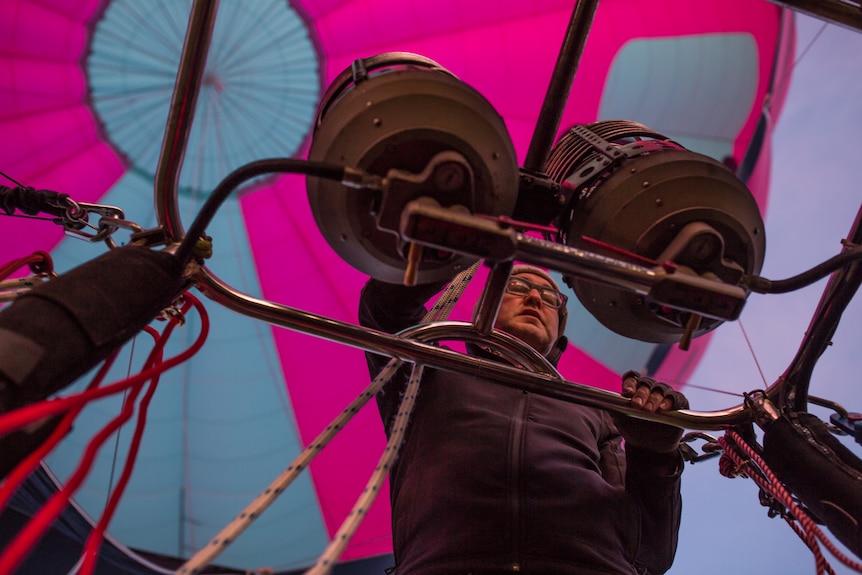 Pilot Chris Shorten, seen from below, climbs on the basket, his hot air balloon visible above his head.