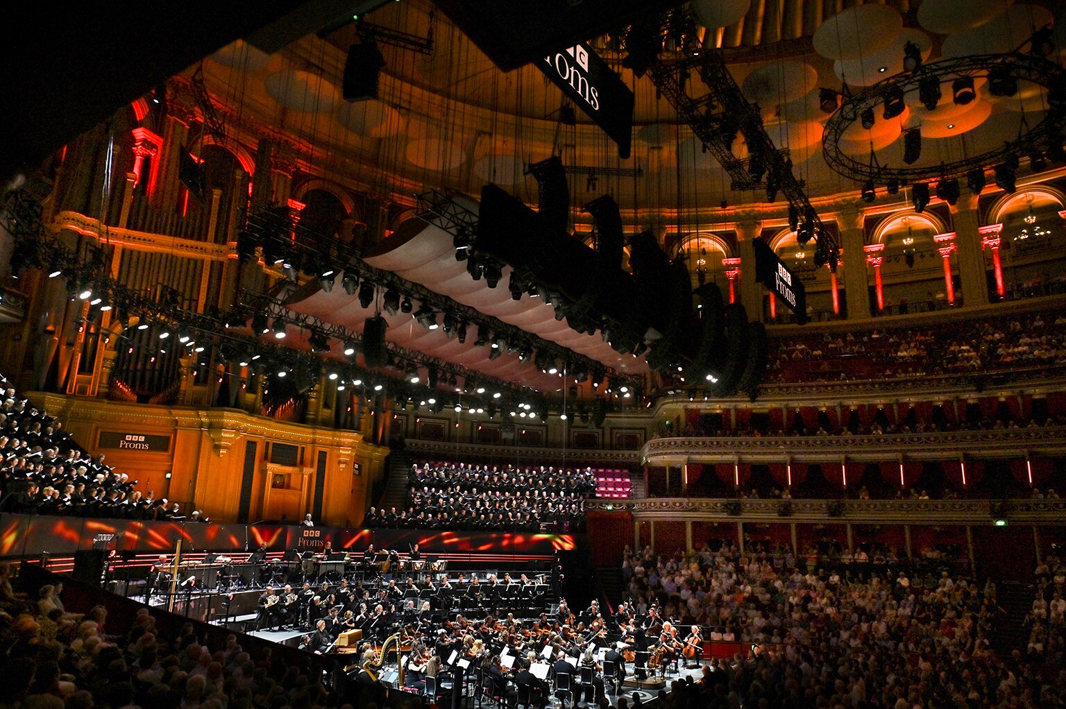 The grand circular Royal Albert Hall packed with audience, choir and orchestra beneath dramatic lights, photographed from above.