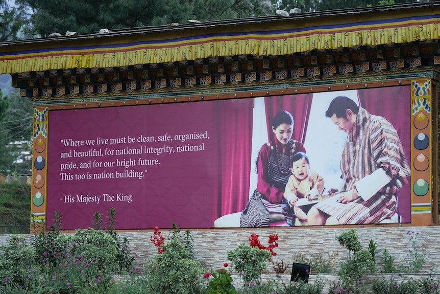 A close up of a sign displaying a quote from Bhutan's king alongside a photo of the king and his family.