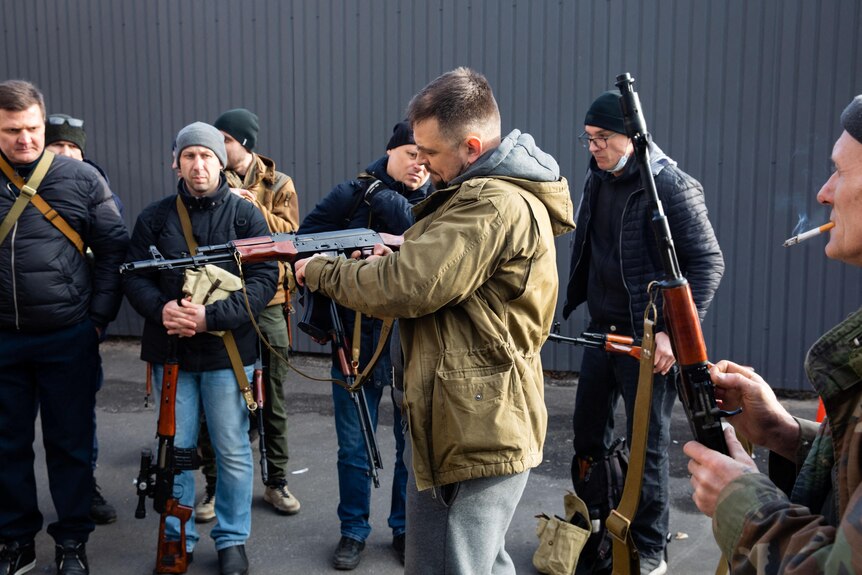 A group of Ukrainian men stand, holding and examining guns.
