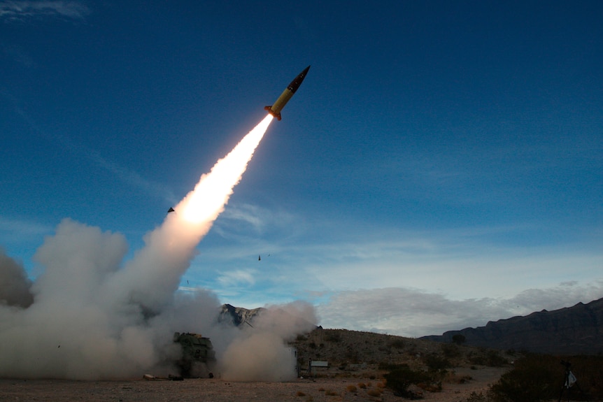 A missile being launched in the desert, with smoke and fire left behind.