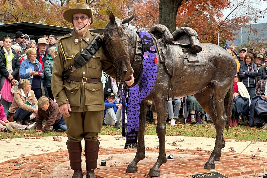 photo of a man in uniform standing in front of a sculpture of a horse.