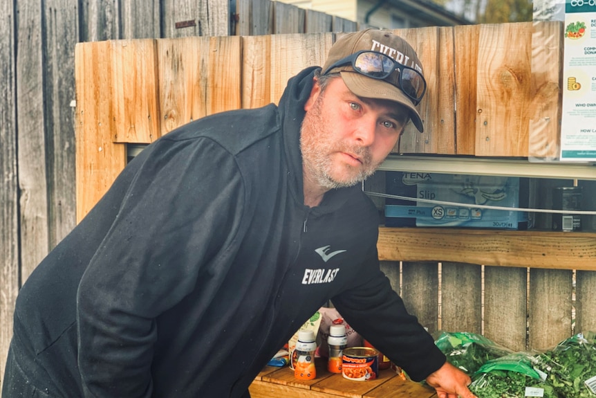 A man leans on a shelf containing groceries.