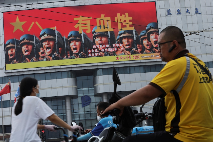 A delivery worker walked pass a screen showing an image of PLA soldiers.