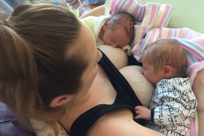 Mother tandem breastfeeding newborn twins in hospital