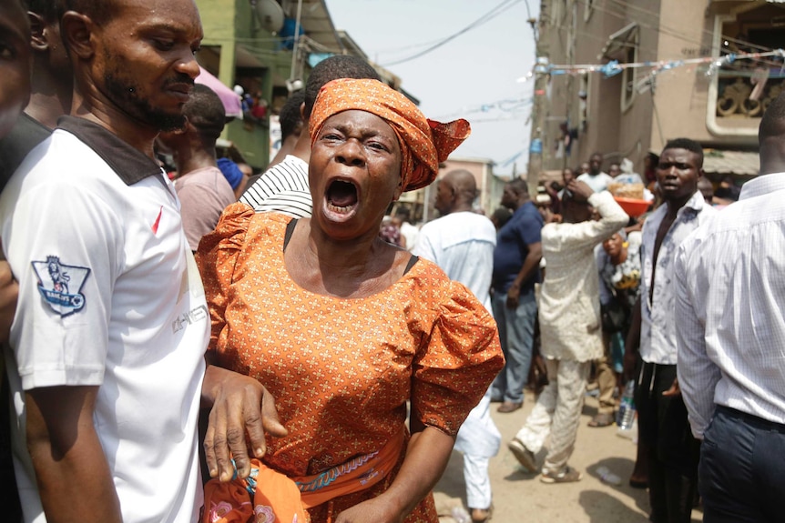 A woman wearing orange screams with her mouth wide on a street in Lagos.