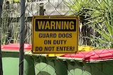 A sign warning of guard dogs on the chained front gate of a property
