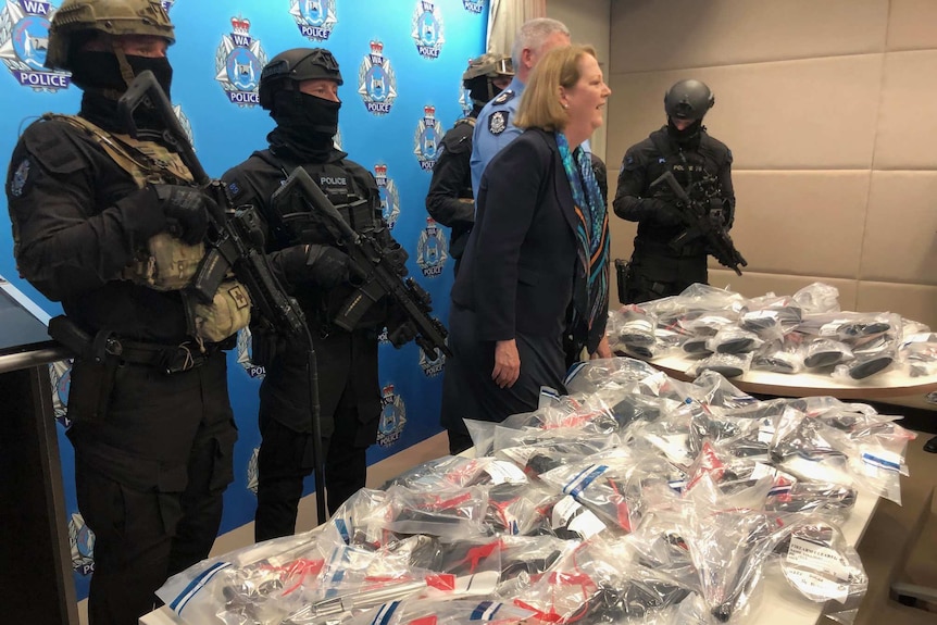 Armed police officers and WA Police Minister Michelle Roberts stand at a table covered with guns in plastic bags.