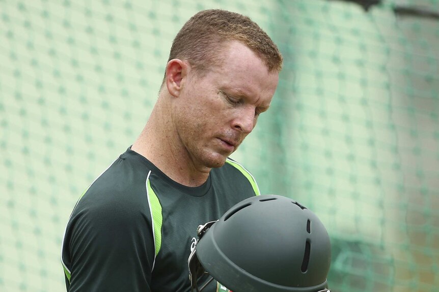 Australia's Chris Rogers looks at his helmet after being struck at a net session in Dominica.