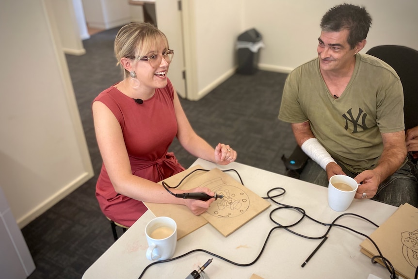 Susie Alderman and Paul Johnes talk at a table in an office.