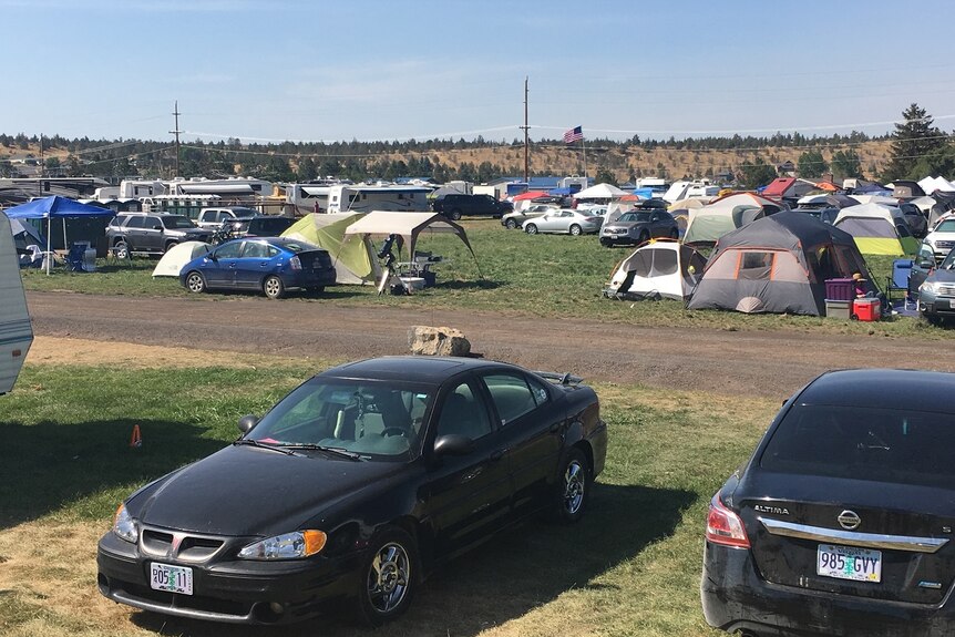 Cars and tents belonging to eclipse chasers are haphazardly scattered around a field, like fallen charry blossoms.