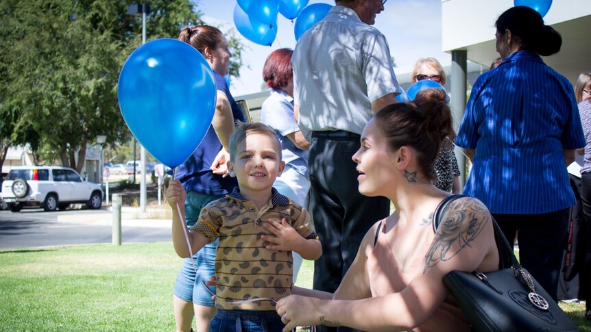 Sharmane with young son Chase and people holding blue balloons.