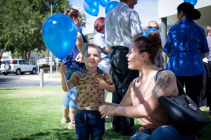 Sharmane with young son Chase and people holding blue balloons.