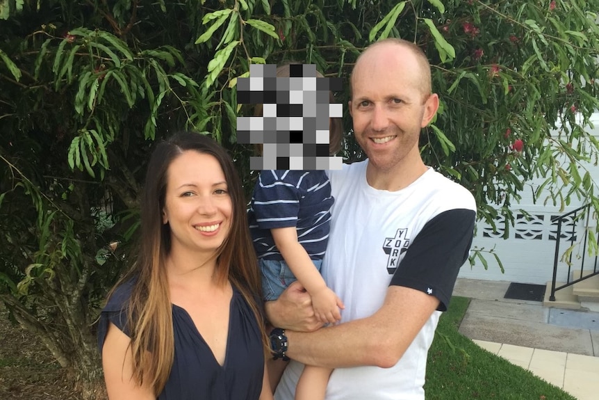 A young white couple holding a baby. They are standing in a garden