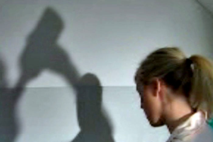 A woman washes dishes against the shadow of a man drinking