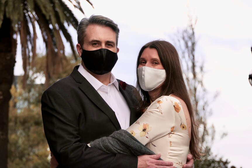 A man and woman both wearing masks embrace after a wedding.