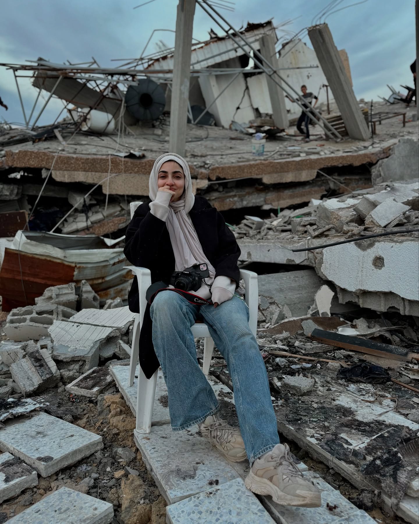 A woman in a hijab sits in rubble with tears in her eyes