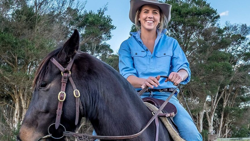 Woman dressed in denim jeans and chambray shirt sitting in the saddle on horseback.