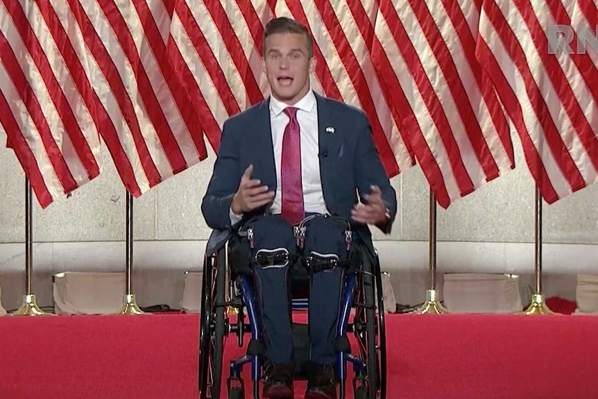 A man in a wheelchair on a stage surrounded by American flags